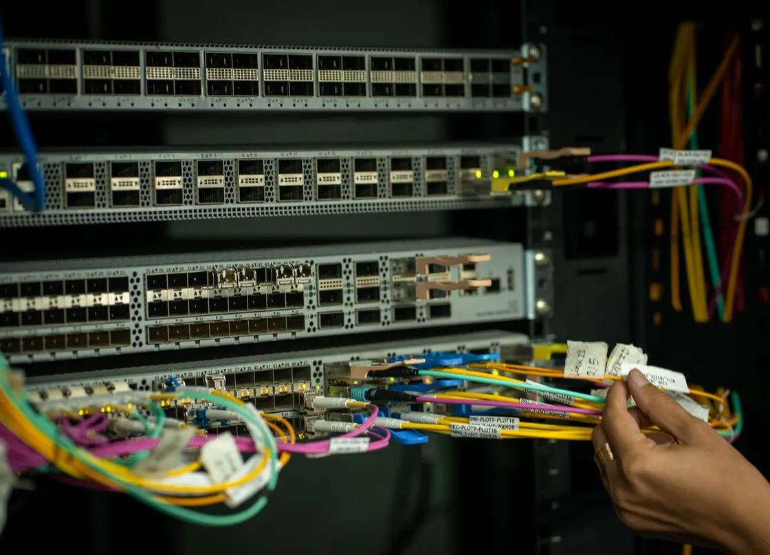 A hand routing fibre optic cables into network switches